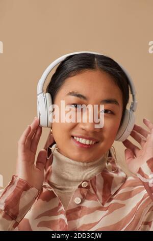 Portrait of Asian young woman in wireless headphone listening to music and smiling at camera Stock Photo