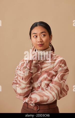 Portrait of Asian young woman with thoughtful sight standing against the beige background Stock Photo