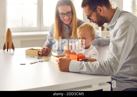 Mom, dad and their little son playing with toy truck together sitting at table at home Stock Photo