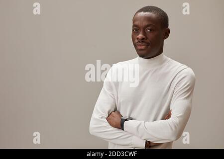 Portrait of African young man in white shirt standing with arms crossed looking at camera against the grey background Stock Photo