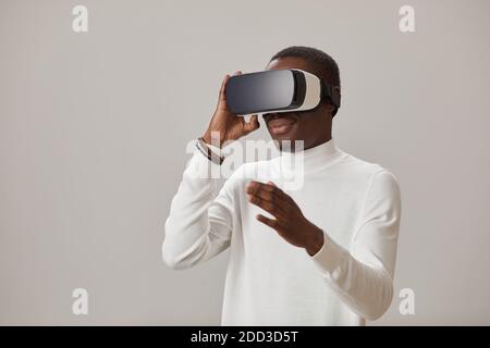 African young man wearing VR glasses and playing in virtual game against the gey background Stock Photo