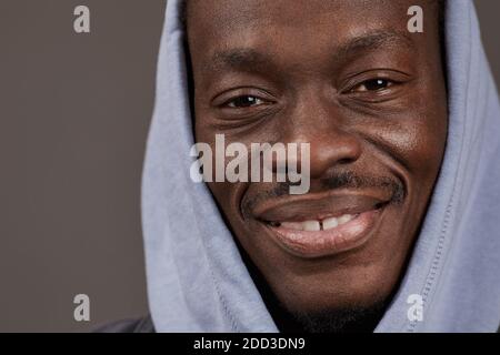 Close-up of African young man in hoody smiling at camera isolated on grey background Stock Photo