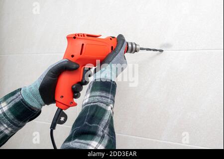 A man's hand drilling a hole in the wall with an electric drill. Stock Photo