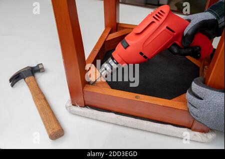 Close-up of man's hand repairing furniture with electric drill in hand. Stock Photo