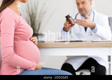Mature experienced doctor showing pills to pregnant lady Stock Photo