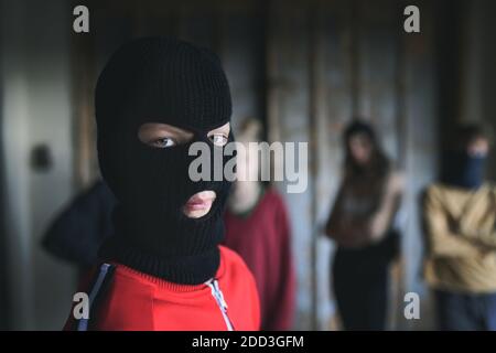 Boy with mask with teenagers gang indoors in abandoned building, looking at camera. Stock Photo