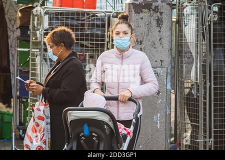 London, UK - 3 November, 2020 - A young mother wearing a face mask while pushing a baby stroller in Walthamstow market Stock Photo