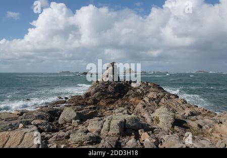 Granite Boulders on the Coast with a Cloudy Blue Sky and Rough Sea Background on the Island of Bryher in the Isles of Scilly, England, UK Stock Photo