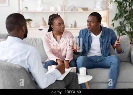 Young Black Spouses Having Relationship Problems, Sitting At Therapy Session With Counselor Stock Photo