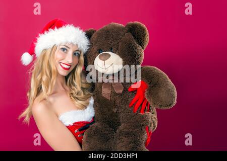 pretty blonde in santa claus dress smiling and happy while hugging a giant teddy bear Stock Photo