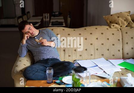 Down syndrome adult man sitting indoors at home, resting on sofa. Stock Photo