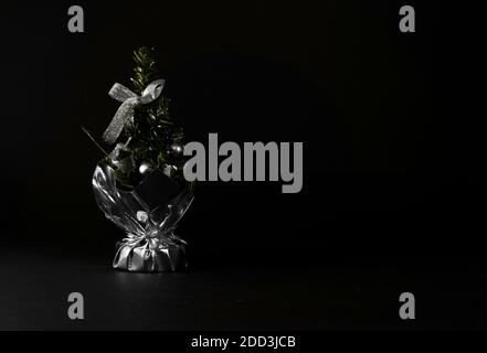 Small Christmas tree in a bag with a bow and decorations. Table accessory with silver decor. Christmas tree on black background for greeting cards Stock Photo