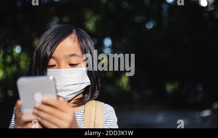 Small Japanese girl with smartphone outdoors in town, coronavirus concept. Stock Photo