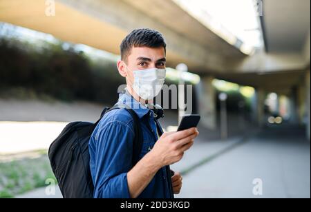 Portrait of young attractive man with smartphone walking outdoors in city, coronavirus concept. Stock Photo