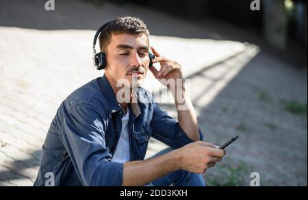 Portrait of young attractive man with smartphone sitting outdoors in city. Stock Photo