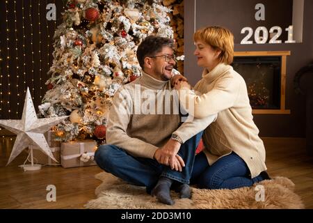Couple in knit sweater sitting on the background of Christmas tree, Happy New Year 2021 Stock Photo