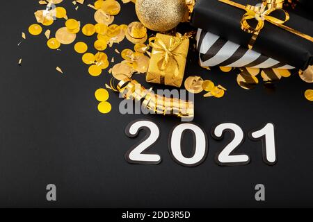 2021 white text lettering on black background with golden confetti, Christmas gift boxes gold balls festive decor. Happy New year event composition. Stock Photo