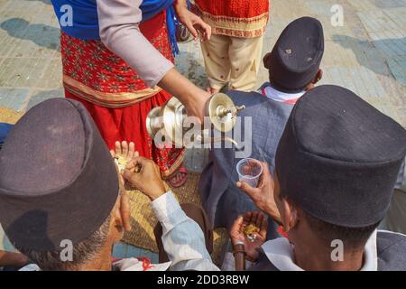 During a Nepalese festival. a woman dispenses drinking water to musicians accompanying a religious procession; Kathmandu, Nepal Stock Photo