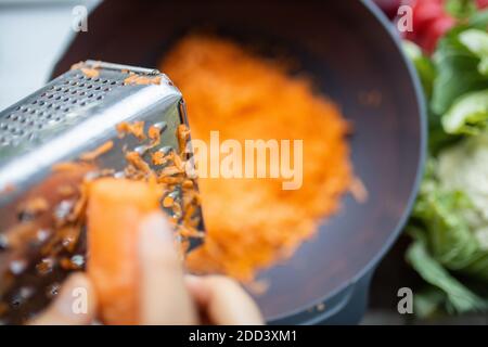 Female hands firmly grating a carrot into a bowl Stock Photo