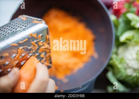 Female hands firmly grating a carrot into a bowl Stock Photo