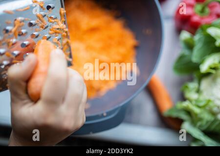 Female hands firmly grating a carrot into a bowl Stock Photo