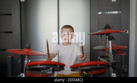 A young boy as a talented drummer of a rock band. A beautiful and cool American teenager plays a drum kit at home. Drummer boy practicing drumming at Stock Photo