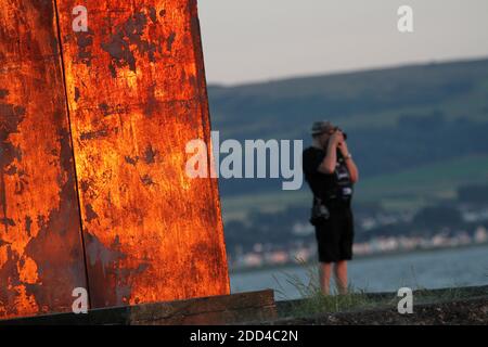 Ayr, Ayrshire, Scotland, UK Abstract Sunlight on metal sculpture at Ayr beach. Donald Urquhart Gateway sculpture on the seafront at Ayr beach marks one end of the River Ayr Way, Ayr, South Ayrshire, Scotland. The structure was made from coal resin obtained from Glenbuck, at the path’s starting point. Tourists and photographers enjoy the evening light against the structure whilst watching the sunset over the Firth of Clyde Stock Photo