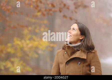 Happy middle age woman contemplating views looking at side in a forest in fall season Stock Photo