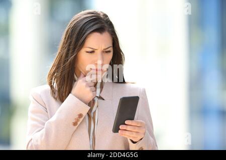 Worried businesswoman reading message on phone walking in the street Stock Photo