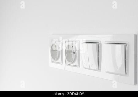 Blurred. White plastic walk-through switches and sockets on a white wall Stock Photo
