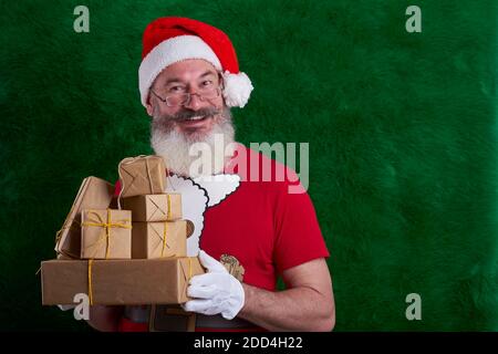 Mature bearded man wearing Santa hat with many gifts in hand, Santa smiling and looking at camera, copy space Stock Photo