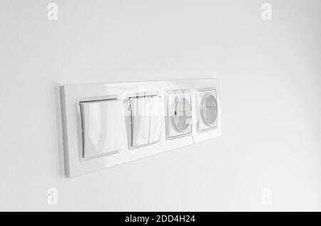 Blurred. White plastic walk-through switches and sockets on a white wall Stock Photo