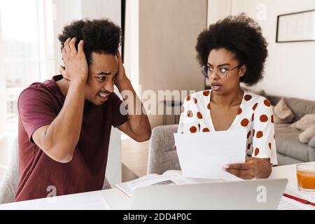 Portrait of worried couple paying bills online via laptop in living room Stock Photo