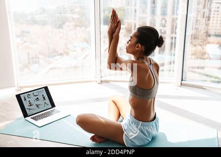 Image of a young concentrated sports african woman using laptop computer and watching videos about exercises indoors Stock Photo