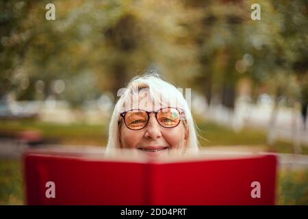 Close up of a woman in glasses is reading a red book while relaxing in the park Stock Photo