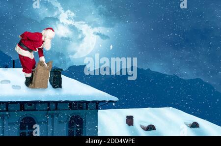 Santa claus stands with backache on a snow-covered roof in a winter landscape Stock Photo