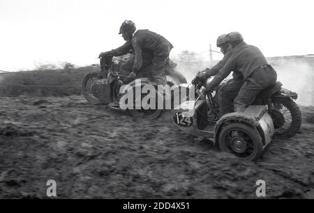 1950s, historical, sidecar motorcycle scrambling......competitors on motorcycles with sidecars in a scrambling or motorcross race on a muddy circuit.. Camberley in Surrey, England was the venue of the first scramble race in 1924. In the following years, the sport grew in popularity, especially in Britain where teams from the classic British motorcycle manufacturers, including the Birmingham Small Arms Company (BSA), Norton, Matchless, Rudge, and AJS competed in races. Stock Photo
