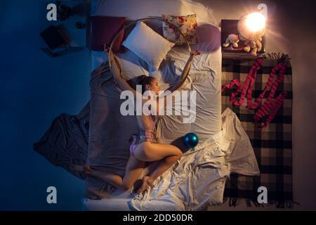 Dreams come true. Top view of young professional rhythmic gymnast sleeping at bedroom in sportwear. Loving sport more than comfort, watching performance even if resting. Action, motion, humor, home. Stock Photo