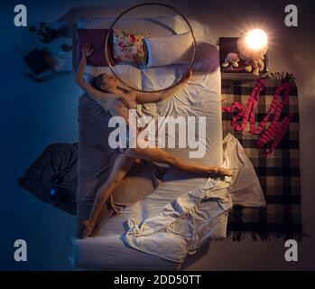 Dreams come true. Top view of young professional rhythmic gymnast sleeping at bedroom in sportwear. Loving sport more than comfort, watching performance even if resting. Action, motion, humor, home. Stock Photo