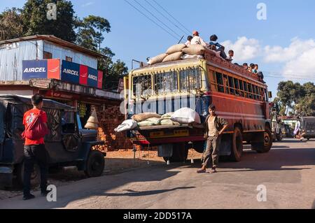 An attendant of a city bus waits for passengers in the small village of Umsning, Meghalaya, India. Passengers are seen sitting on the top of the bus. Stock Photo