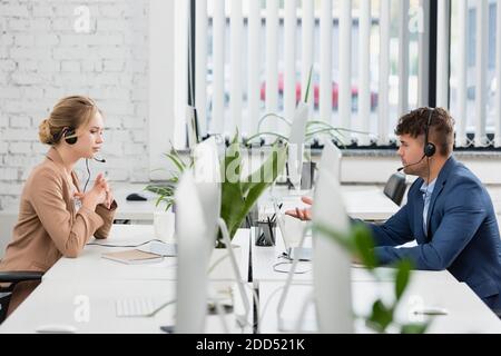 Call center operators in headsets working, while sitting at table with digital devices in office on blurred foreground Stock Photo