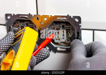 The guy checks the voltage in the disassembled electrical outlet with a multimeter Stock Photo