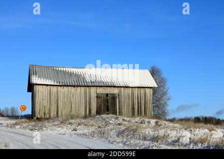 Old country barn under clear blue sky by rural road in early winter. Stock Photo