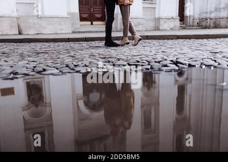 cropped photo of Happy young stylish couple, enjoying their hugging in old road in city street with ancient building on the background. after rain Stock Photo