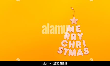 Text Merry Christmas in shape of fir tree made from wooden letters on orange background Stock Photo