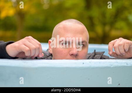 Serious young man looking at camera over rim of a tank or outdoor pool at a park with a happy friendly grin Stock Photo