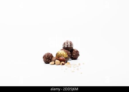 Close up of wrapped and unwrapped chocolate and hazelnut sweets with raw hazelnuts on a light background. Chocolate sweets and abstract concept. Stock Photo