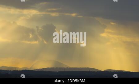 Silhouette of a hills against beautiful golden hour light and beautiful clouds formation with rays of sunlight breaking Stock Photo