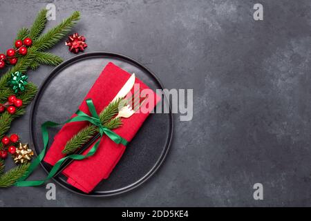 Christmas table setting with black ceramic plate, fir tree branch and gold and red accessories on black stone background. Top view. Copy space - Image Stock Photo
