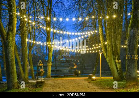 Park or garden with warm light bulbs, street lamps at evening or night, decorative illumination, celebration, cozy Christmas background Stock Photo